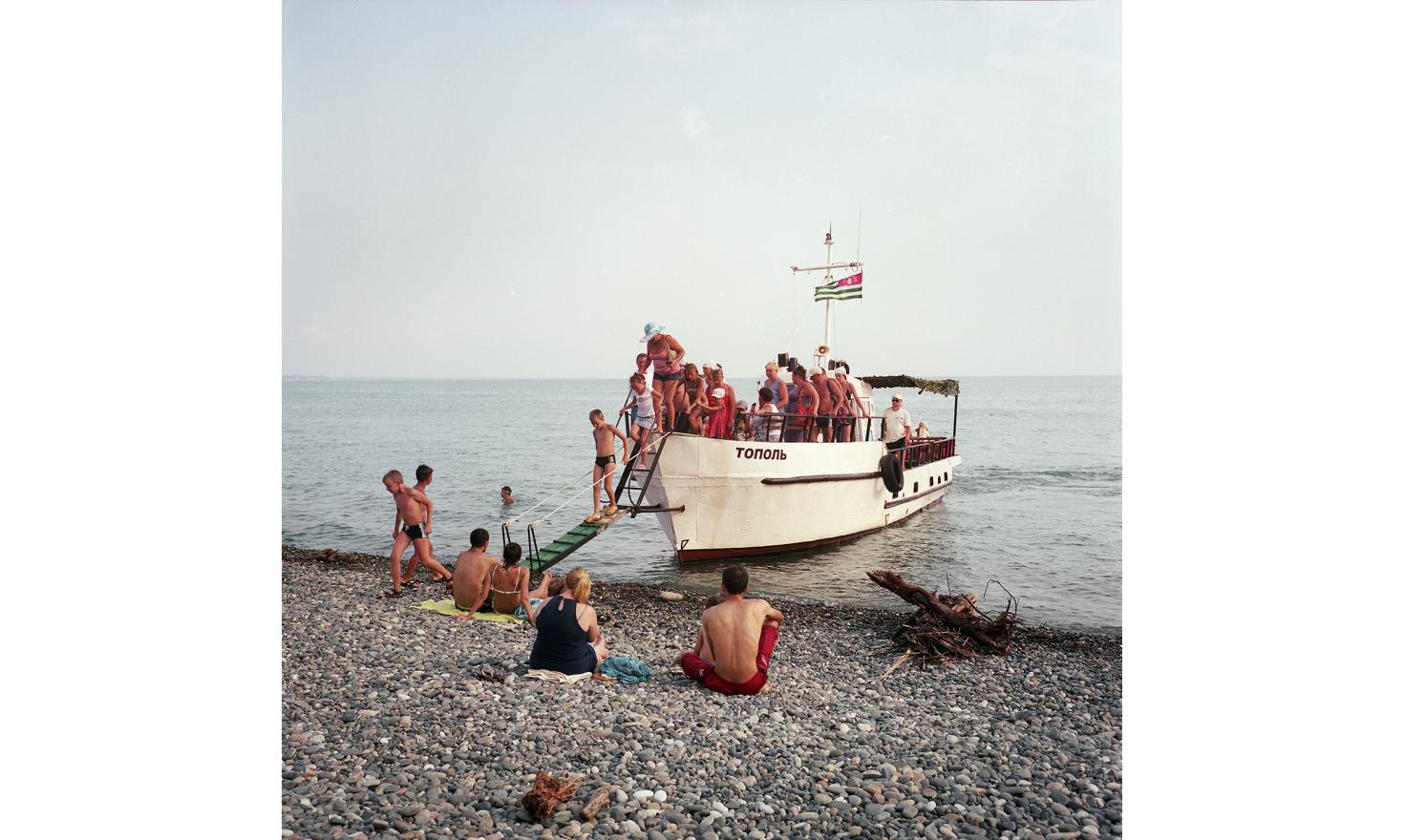 On the beach in Gagra. A boat comes take the tourists for an hour trip. The boat's captain was working on large fishing vessels in the past. Today, he renovated this boat and works for tourists.
