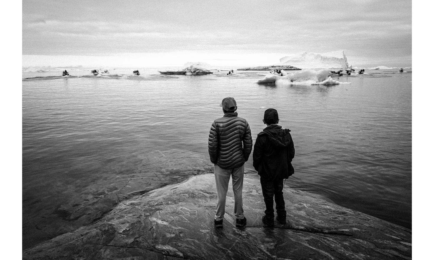 De jeunes adolescents regardent le départ de la course à la chasse au phoque, le 21 juin, jour du solstice d’été et fête nationale groenlandaise. Les jeunes sont partagés entre l’envie de rester au Groenland et le désir d’ailleurs. (...)